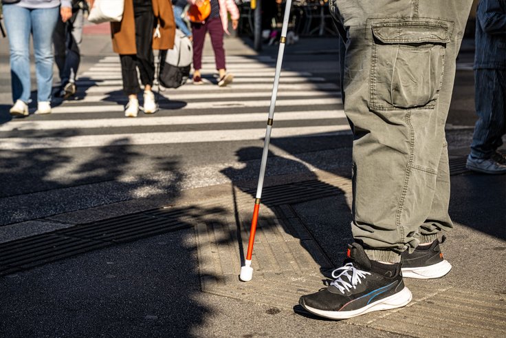 Person mit Blindenstock vor Zebrastreifen bei taktilem Bodenleitsystem